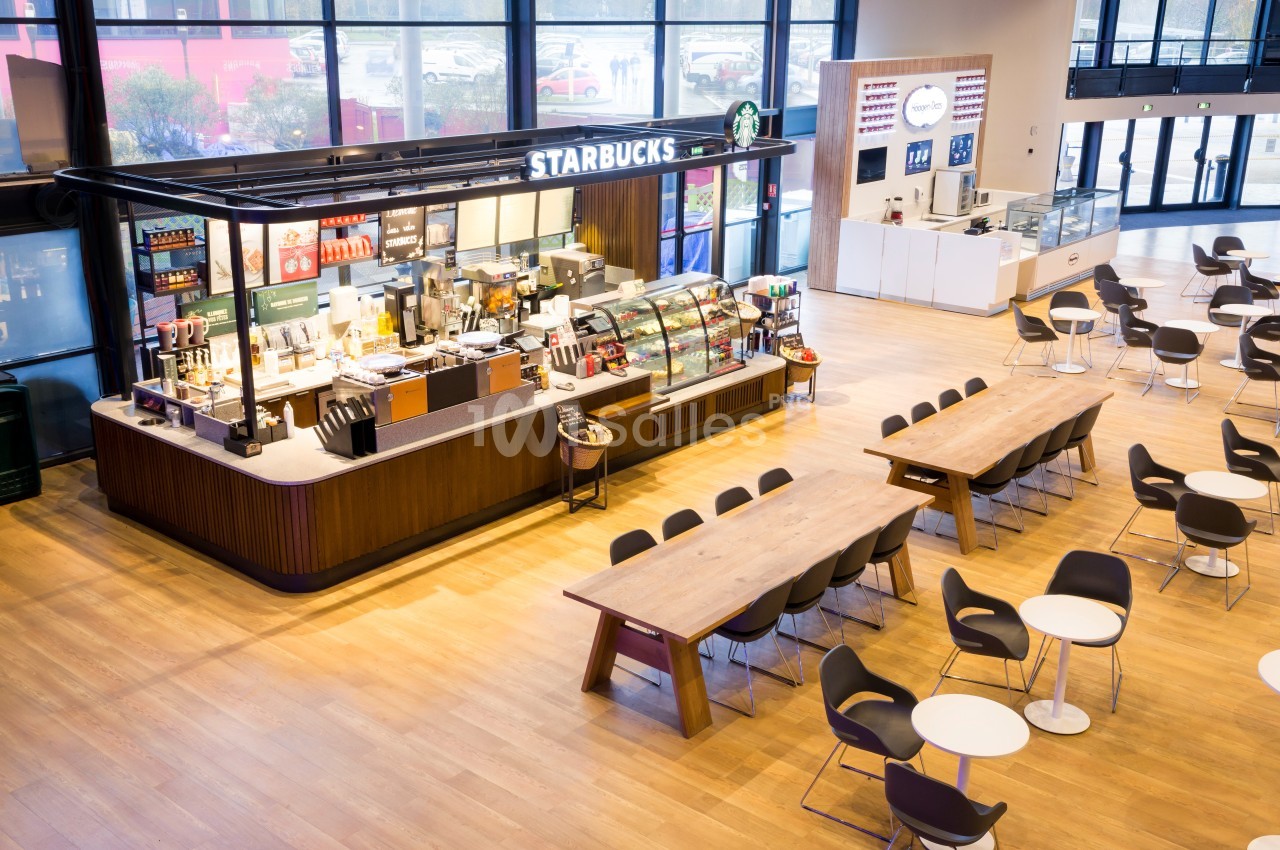 Comptoir Starbucks dans un espace lumineux avec tables, chaises et grandes baies vitrées en arrière-plan.