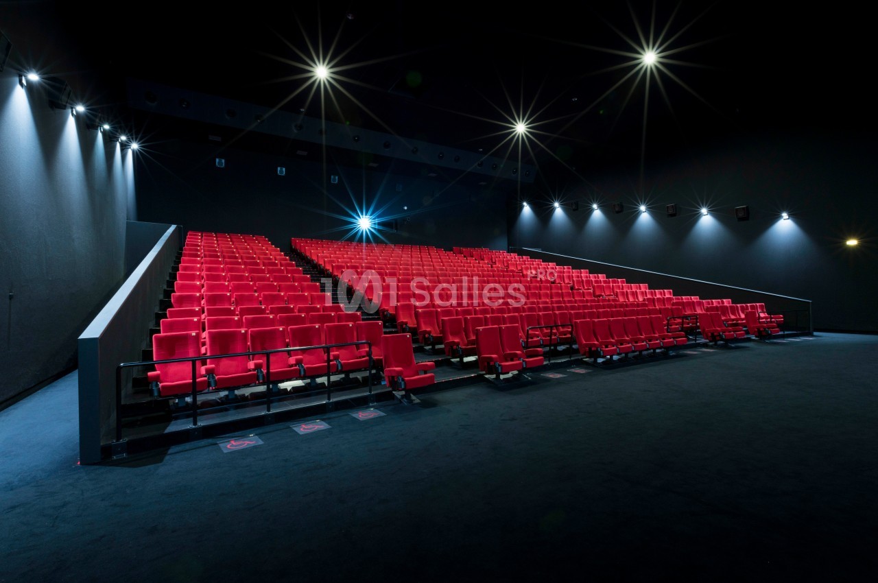 Salle de cinéma vide avec des rangées de sièges rouges et un éclairage tamisé.