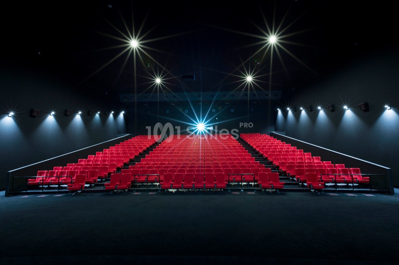Salle de cinéma vide avec des rangées de sièges rouges et un projecteur allumé au fond.