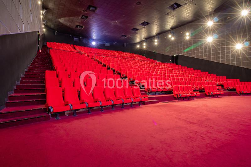 Salle de cinéma vide avec rangées de sièges rouges et éclairage tamisé.