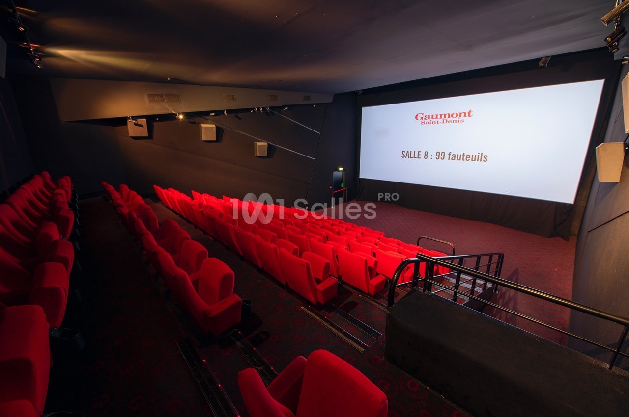 Salle de cinéma vide avec des fauteuils rouges, écran blanc affichant ’Gaumont’ et la capacité de 99 fauteuils.