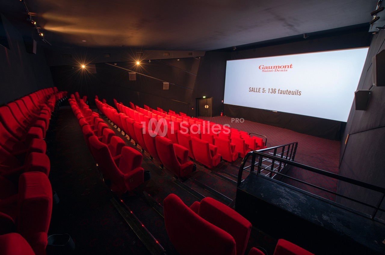 Salle de cinéma vide avec rangées de fauteuils rouges et écran affichant des informations sur la capacité.