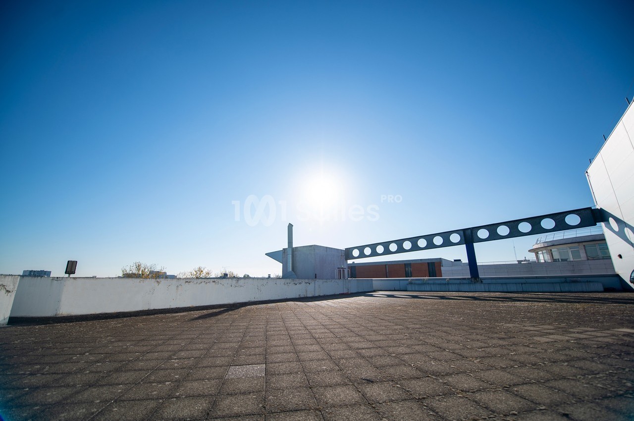 Toit-terrasse ensoleillé avec sol en dalles, balustrade moderne et ciel bleu dégagé en arrière-plan.