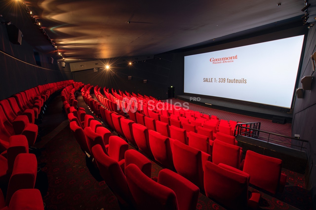 Salle de cinéma avec des rangées de fauteuils rouges vides et un grand écran affichant des informations sur la capacité.