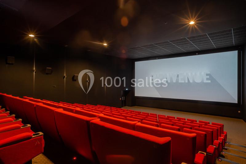 Salle de cinéma vide avec des sièges rouges et un écran affichant le mot ’Bienvenue’.