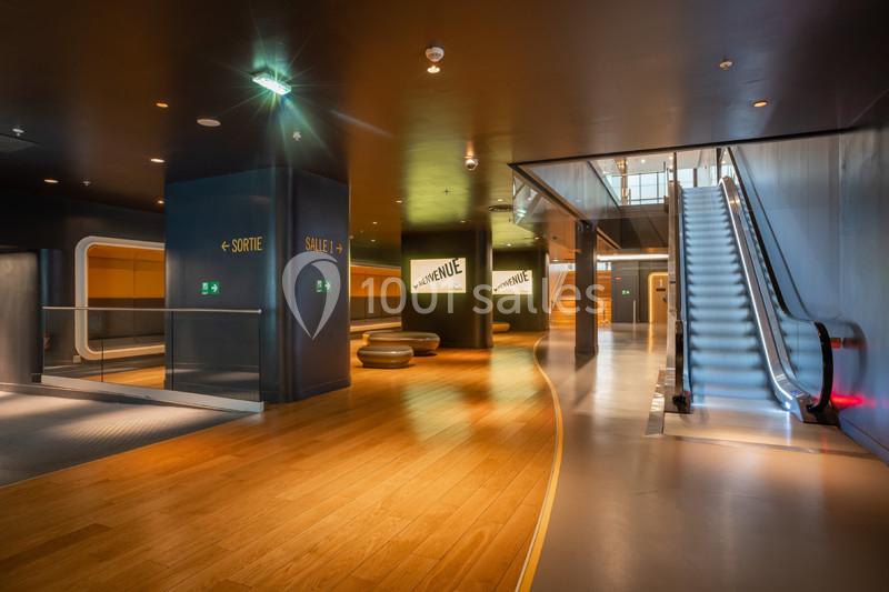 Hall moderne avec sol en bois, escalier mécanique, panneaux de signalisation et éclairage tamisé.