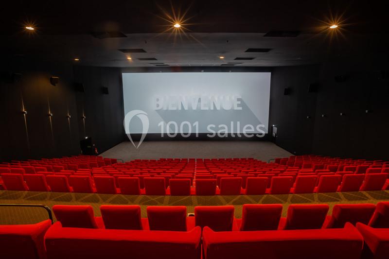 Salle de cinéma vide avec des rangées de sièges rouges et un écran affichant le mot ’Bienvenue’.