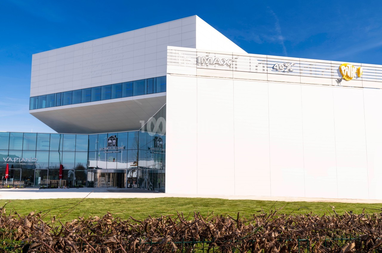 Façade d'un bâtiment moderne avec des enseignes de cinéma IMAX et 4DX, entouré d'une pelouse et d'arbustes.