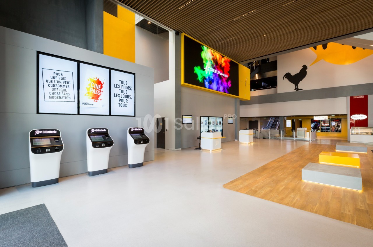 Hall moderne avec bornes interactives, affiches murales, écrans numériques et espaces d’accueil lumineux.
