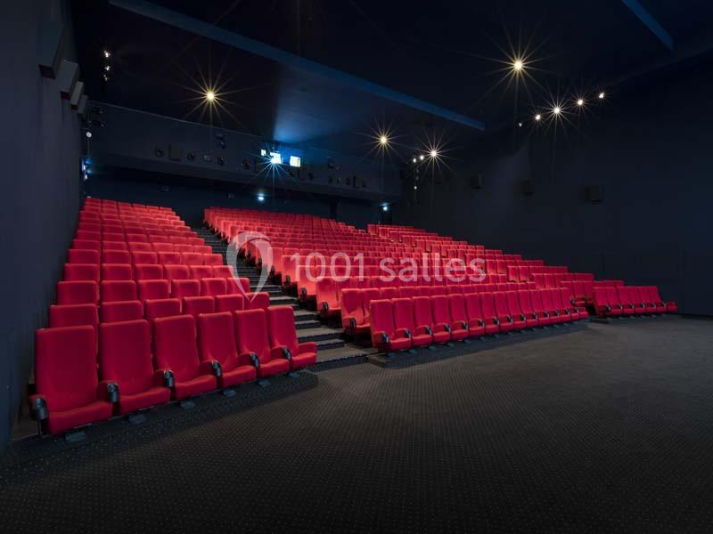 Salle de cinéma vide avec des rangées de sièges rouges et un éclairage tamisé.