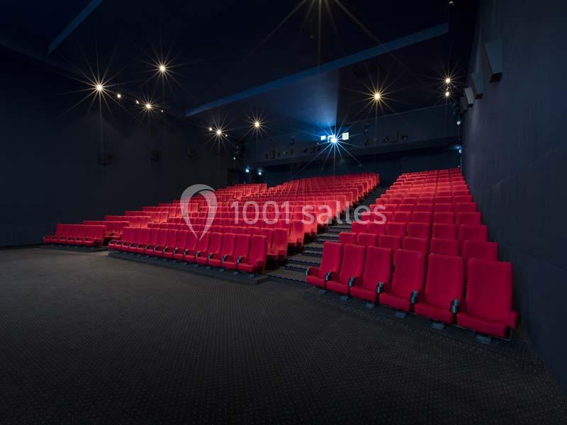 Salle de cinéma vide avec des rangées de sièges rouges et un éclairage tamisé.