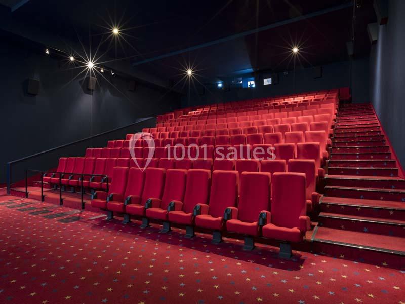 Salle de cinéma vide avec des rangées de sièges rouges et un sol recouvert d'une moquette étoilée.