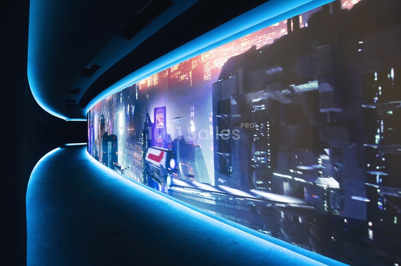 Couloir futuriste avec un écran incurvé affichant une scène urbaine nocturne aux néons, éclairé par une lumière bleue.