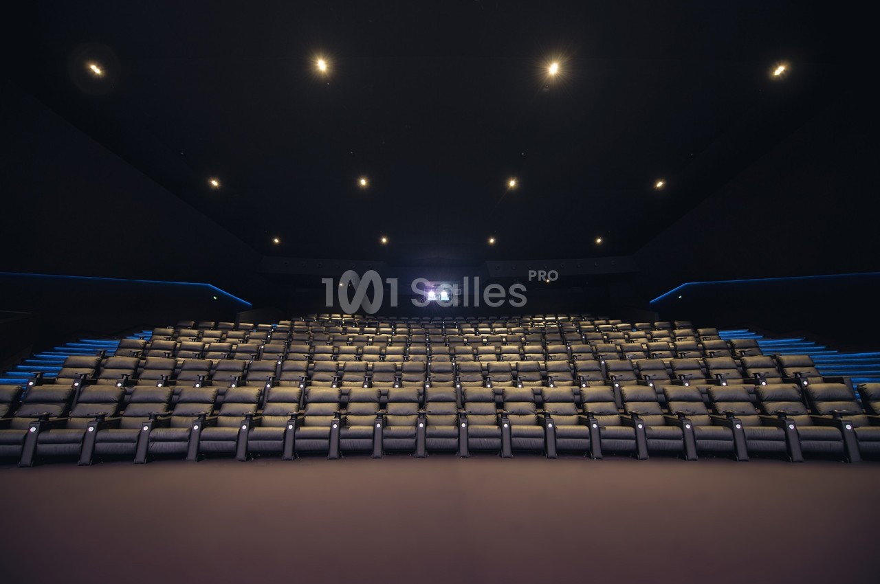 Salle de cinéma vide avec des rangées de sièges en cuir beige, éclairée par des lumières tamisées au plafond.