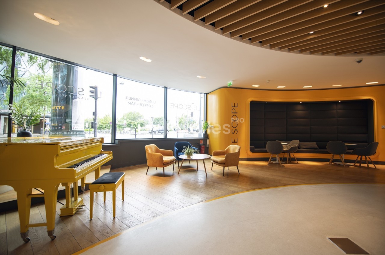 Espace lumineux avec un piano jaune, des fauteuils modernes et une grande baie vitrée donnant sur l'extérieur.
