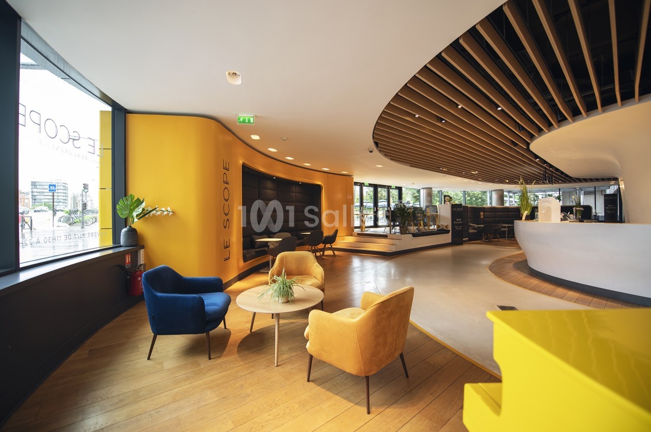 Espace intérieur moderne avec fauteuils colorés, table basse, murs jaunes et plafond avec lattes en bois.