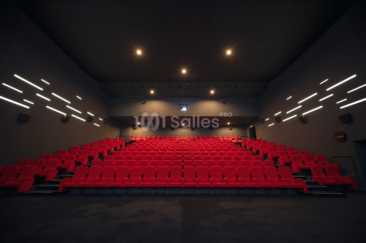 Salle de cinéma vide avec des rangées de sièges rouges et un éclairage tamisé au plafond.