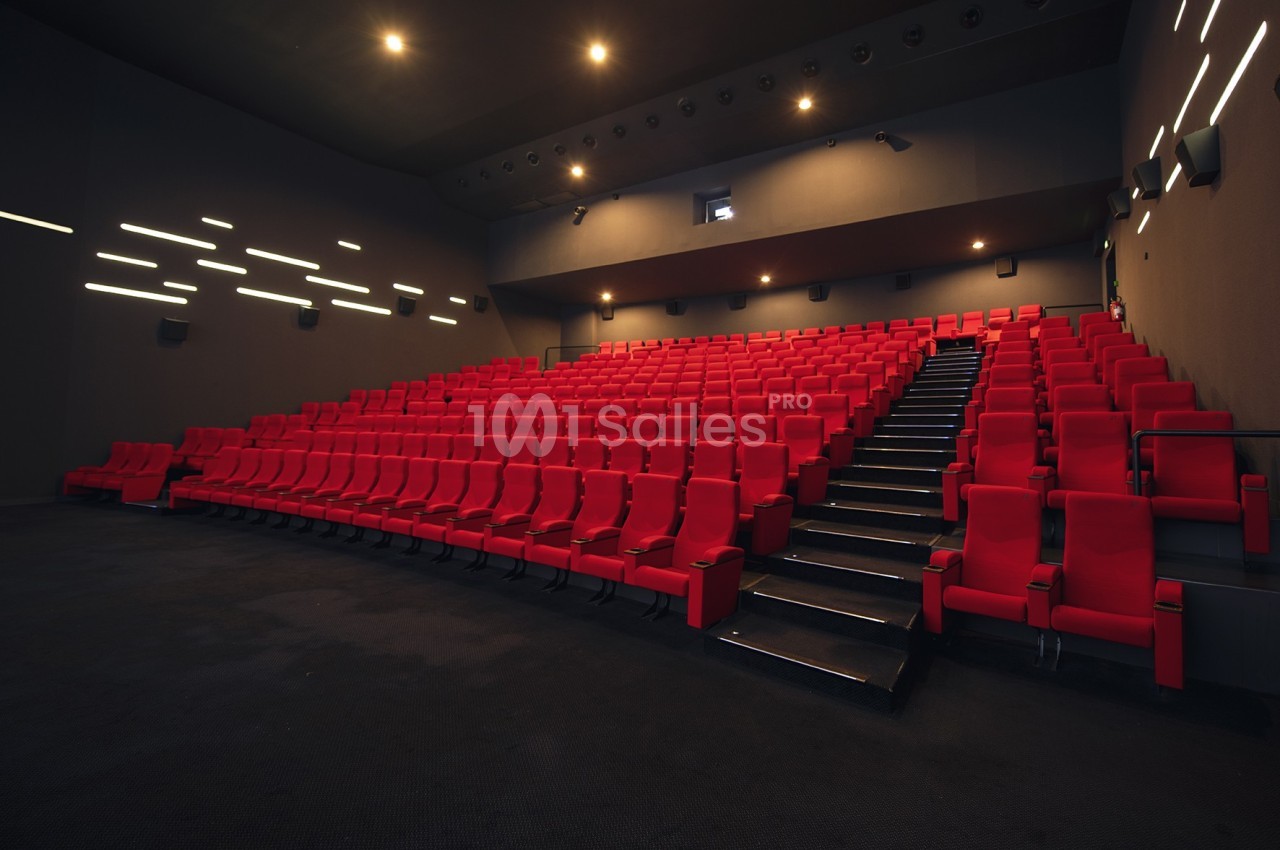 Salle de cinéma vide avec des rangées de sièges rouges et un éclairage tamisé sur les murs.
