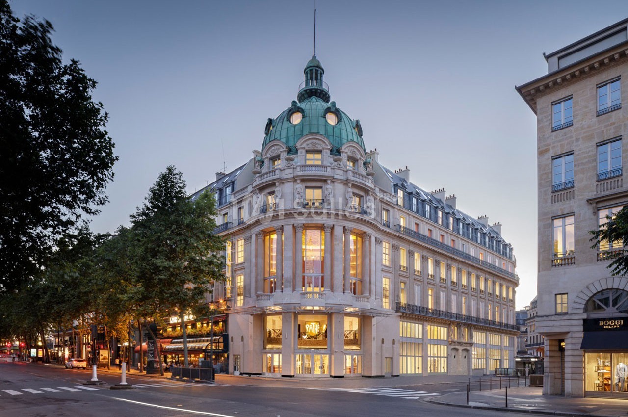 Bâtiment haussmannien avec coupole verte, éclairé à la tombée de la nuit, situé à un carrefour parisien.
