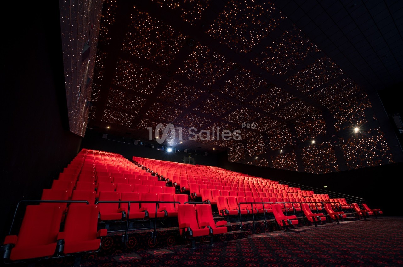 Salle de cinéma vide avec des rangées de sièges rouges et un plafond illuminé par des lumières étoilées.