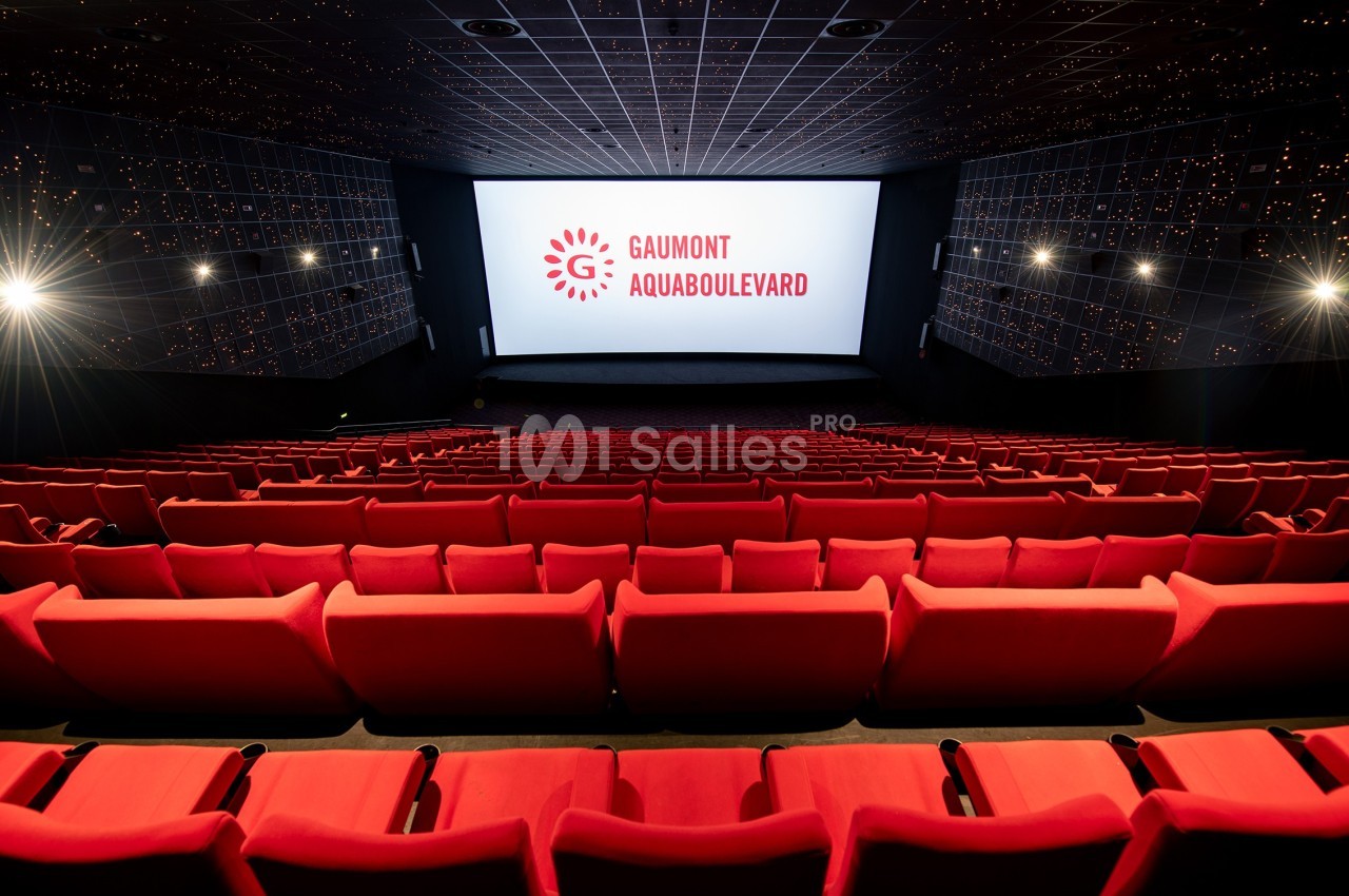 Salle de cinéma vide avec rangées de sièges rouges et écran affichant ’Gaumont Aquaboulevard’.