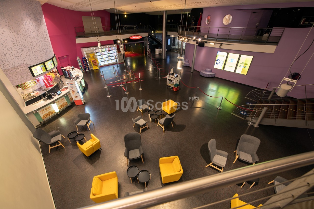 Vue d'un espace d'accueil moderne avec fauteuils colorés, comptoir de confiserie et escalier menant à un étage.