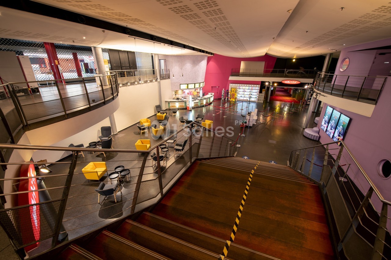 Vue intérieure d'un espace public moderne avec escalier central, sièges colorés et comptoirs de restauration.