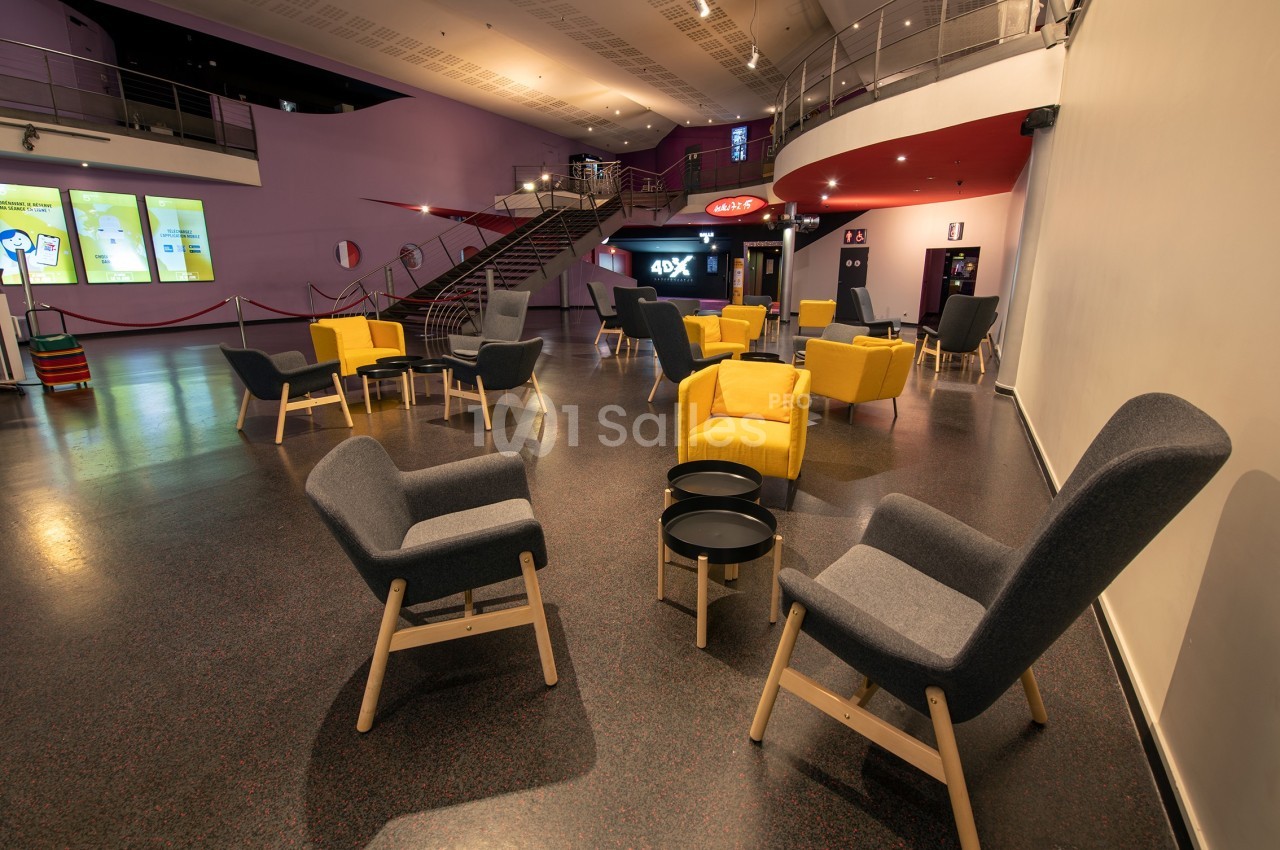 Espace d'attente moderne avec fauteuils gris et jaunes, tables basses noires et éclairage intérieur chaleureux.