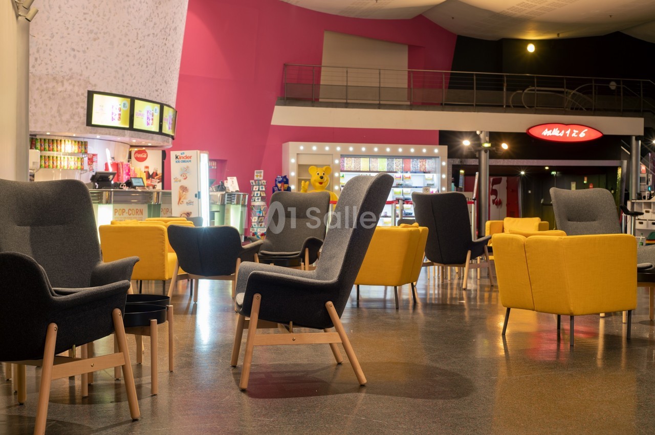 Espace détente avec fauteuils colorés et tables basses dans un hall lumineux, près d'un comptoir de snacks.