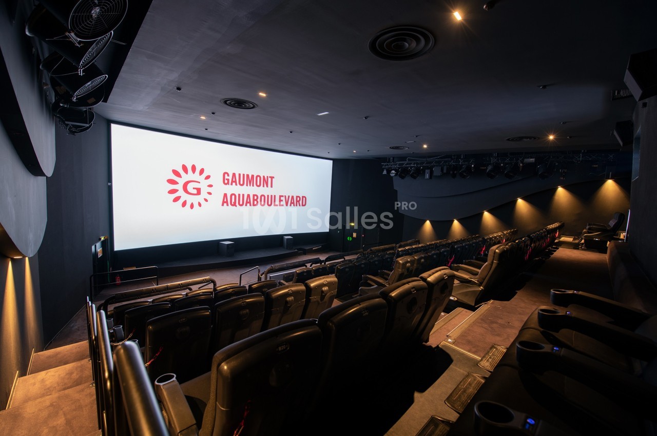 Salle de cinéma moderne avec sièges inclinés, écran géant affichant le logo ’Gaumont Aquaboulevard’.