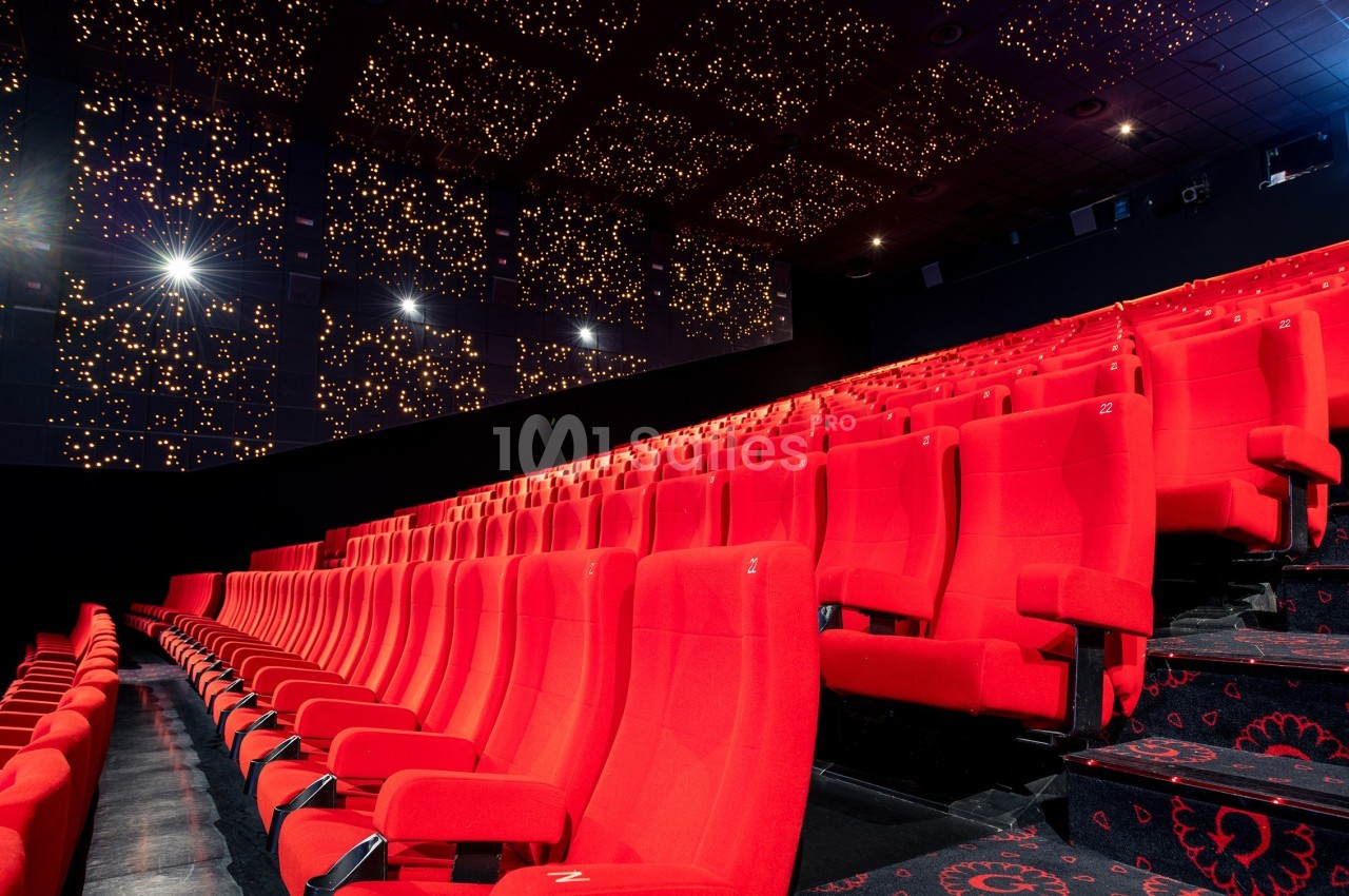 Salle de cinéma vide avec des rangées de fauteuils rouges et un plafond décoré de lumières étoilées.