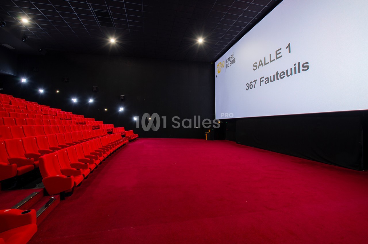 Salle de cinéma avec écran géant, rangées de fauteuils rouges et moquette assortie, éclairage tamisé.