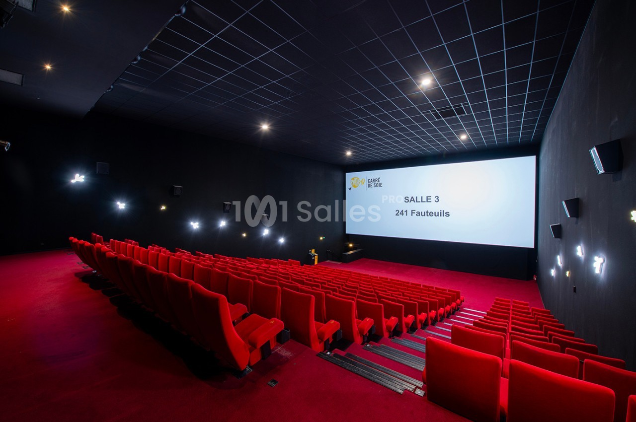 Salle de cinéma vide avec des fauteuils rouges, écran blanc affichant ’Salle 3 - 241 fauteuils’, éclairage tamisé.