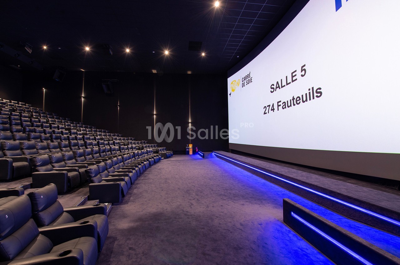 Salle de cinéma moderne avec écran large, rangées de fauteuils en cuir et éclairage tamisé.