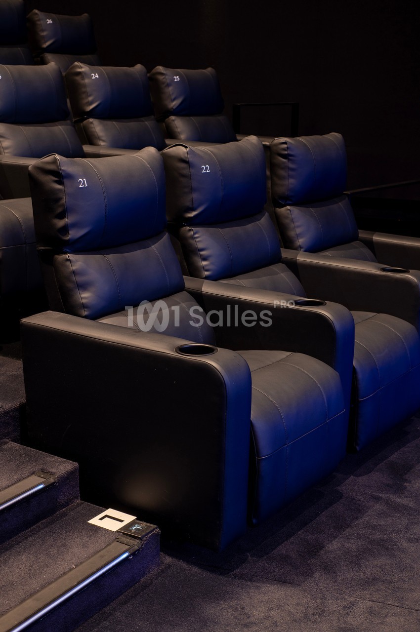 Fauteuils de cinéma en cuir noir numérotés, avec accoudoirs et porte-gobelets, disposés en gradins.