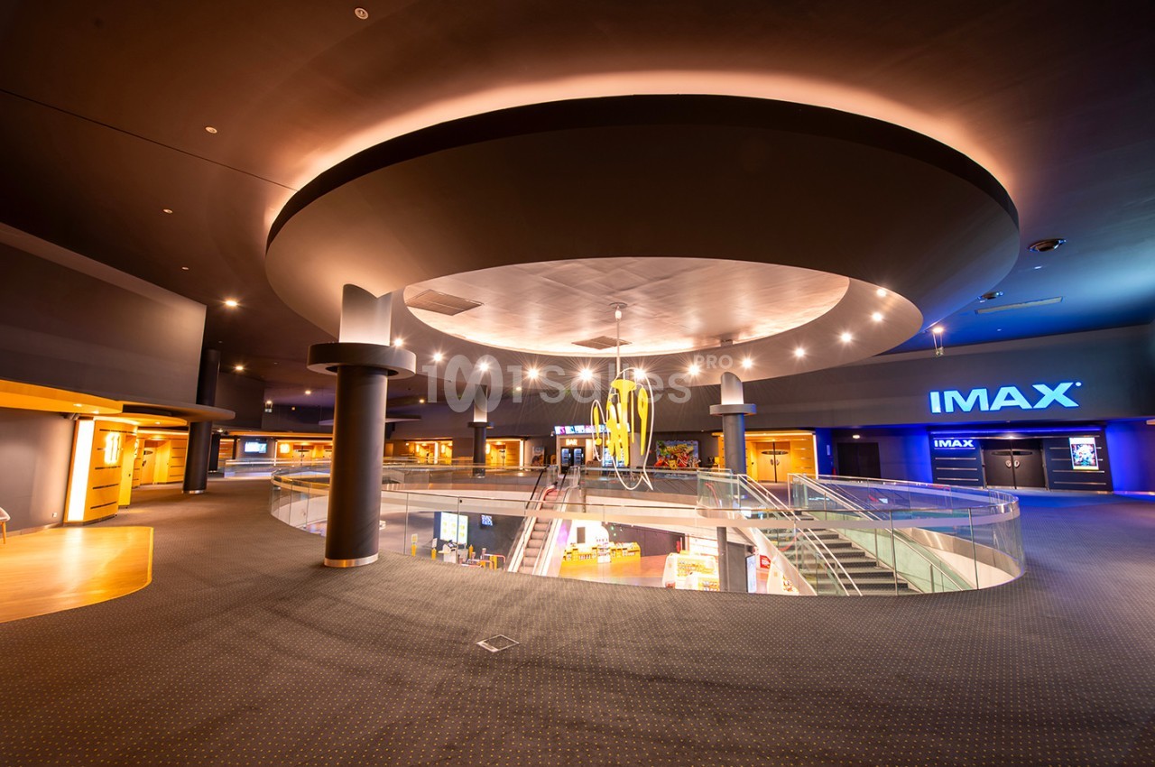 Hall d'entrée spacieux d'un cinéma avec escalier, éclairage moderne et enseigne IMAX visible au fond.