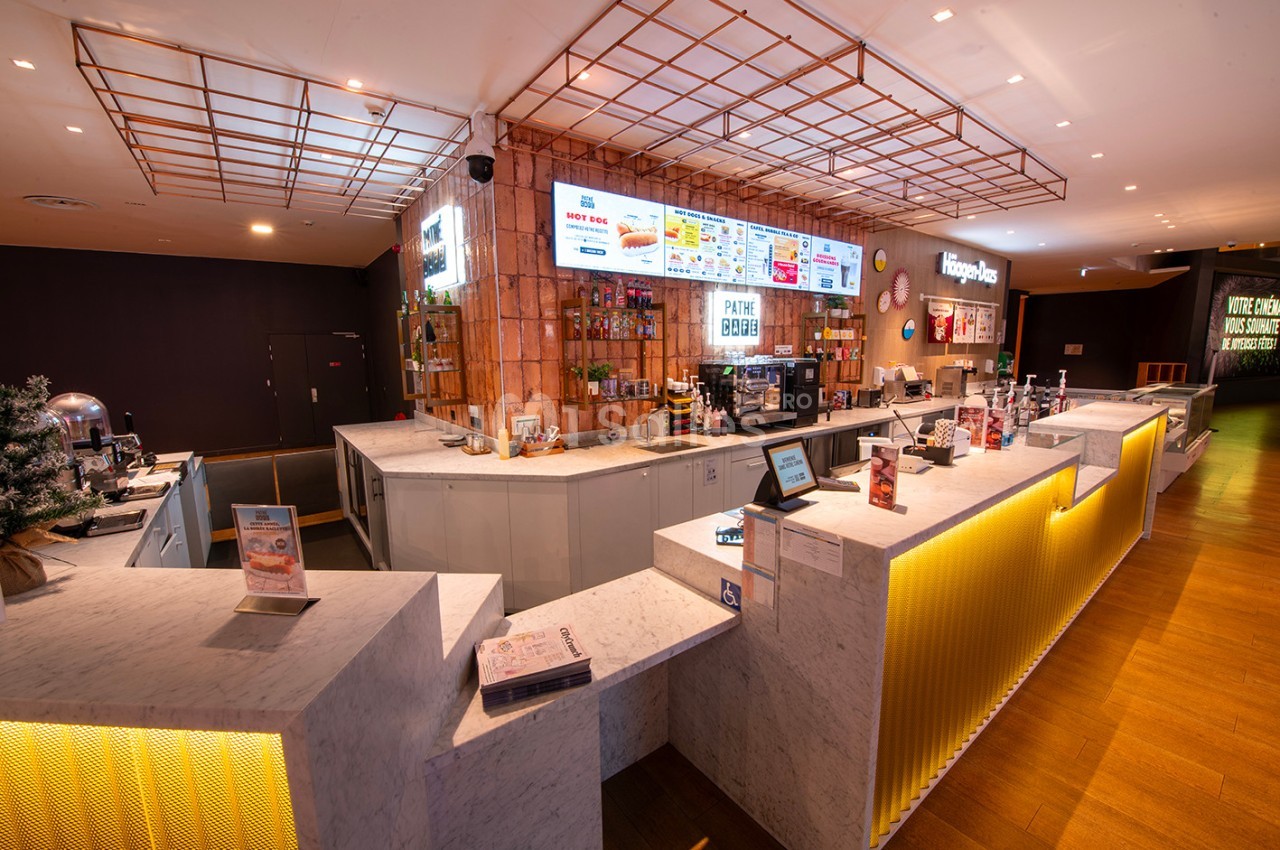 Comptoir moderne d'un cinéma avec menus affichés, machines à boissons et présentoirs de snacks.