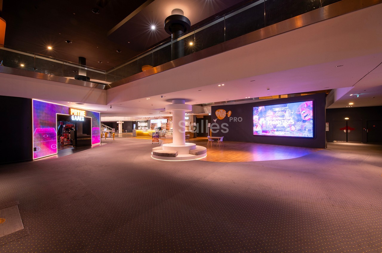 Espace intérieur moderne avec éclairage tamisé, écran géant lumineux et zone de jeux colorée sur la gauche.