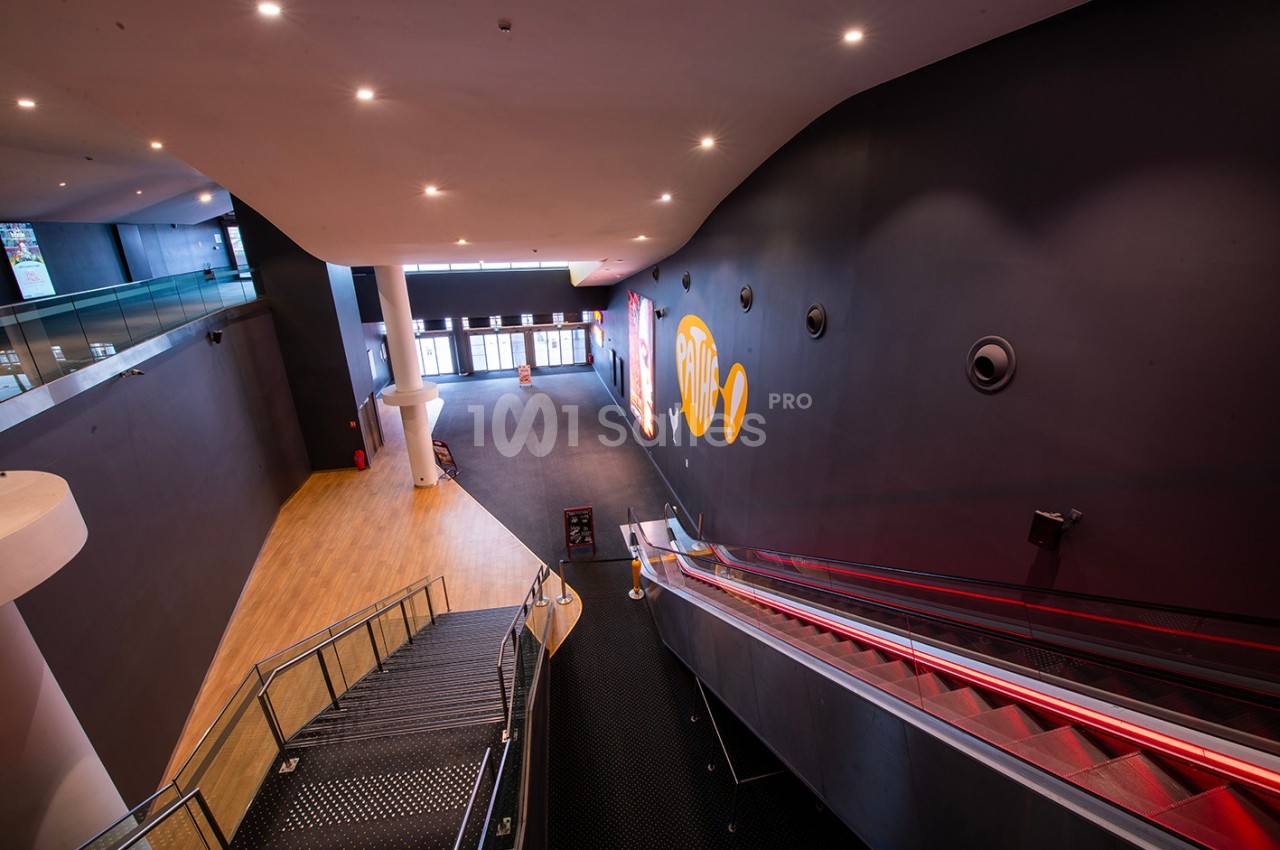 Vue intérieure d'un espace moderne avec escalier, escalator rouge et murs sombres décorés de motifs colorés.