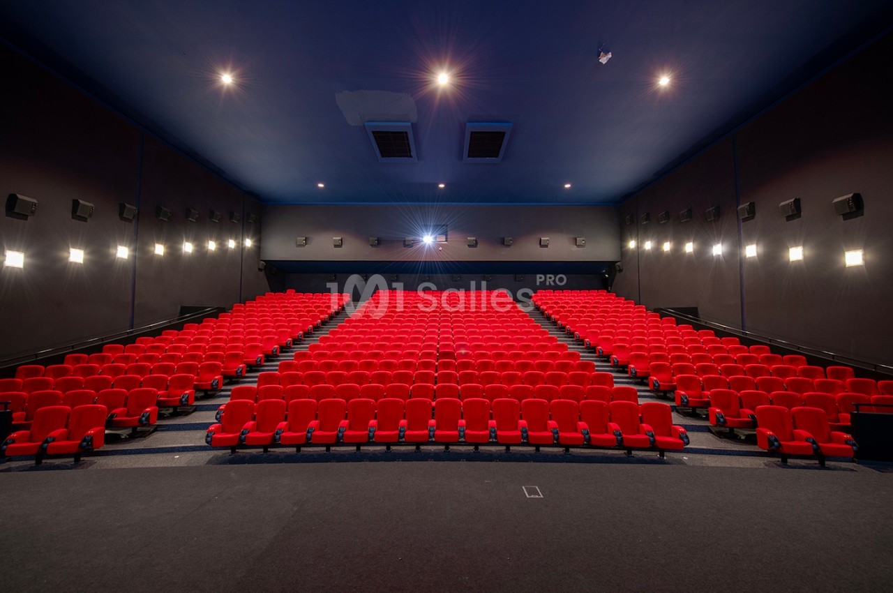 Salle de cinéma vide avec des rangées de fauteuils rouges et un écran blanc en arrière-plan.