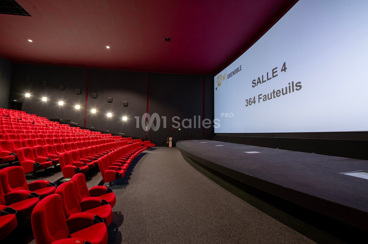 Salle de cinéma vide avec des fauteuils rouges, un grand écran affichant ’Salle 4, 364 fauteuils’ et un éclairage tamisé.