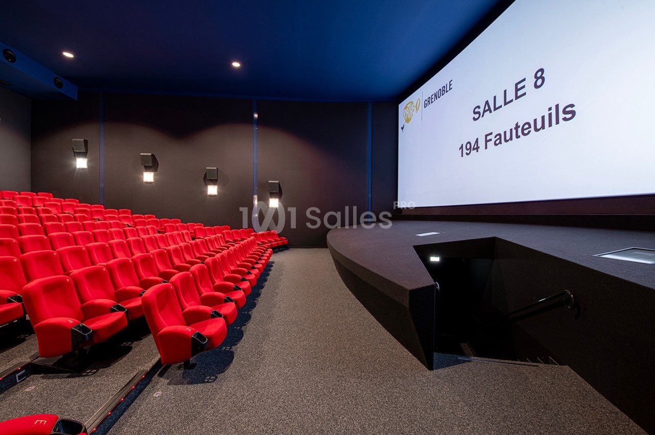 Salle de cinéma moderne avec sièges rouges, écran géant affichant ’Salle 8, 194 fauteuils’ et éclairage mural discret.