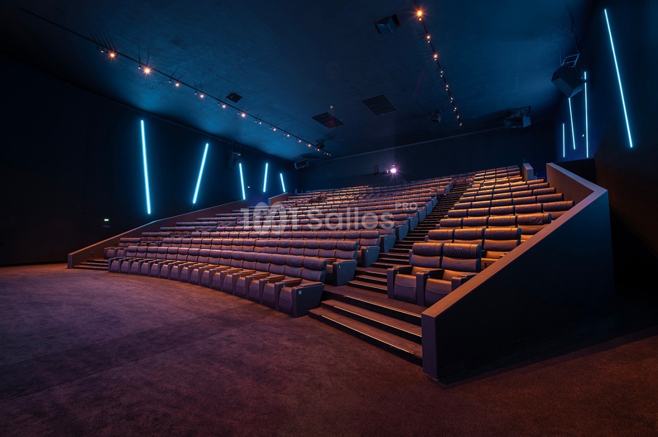 Salle de cinéma vide avec sièges inclinés en gradins, éclairage tamisé et lumières LED bleues sur les murs.