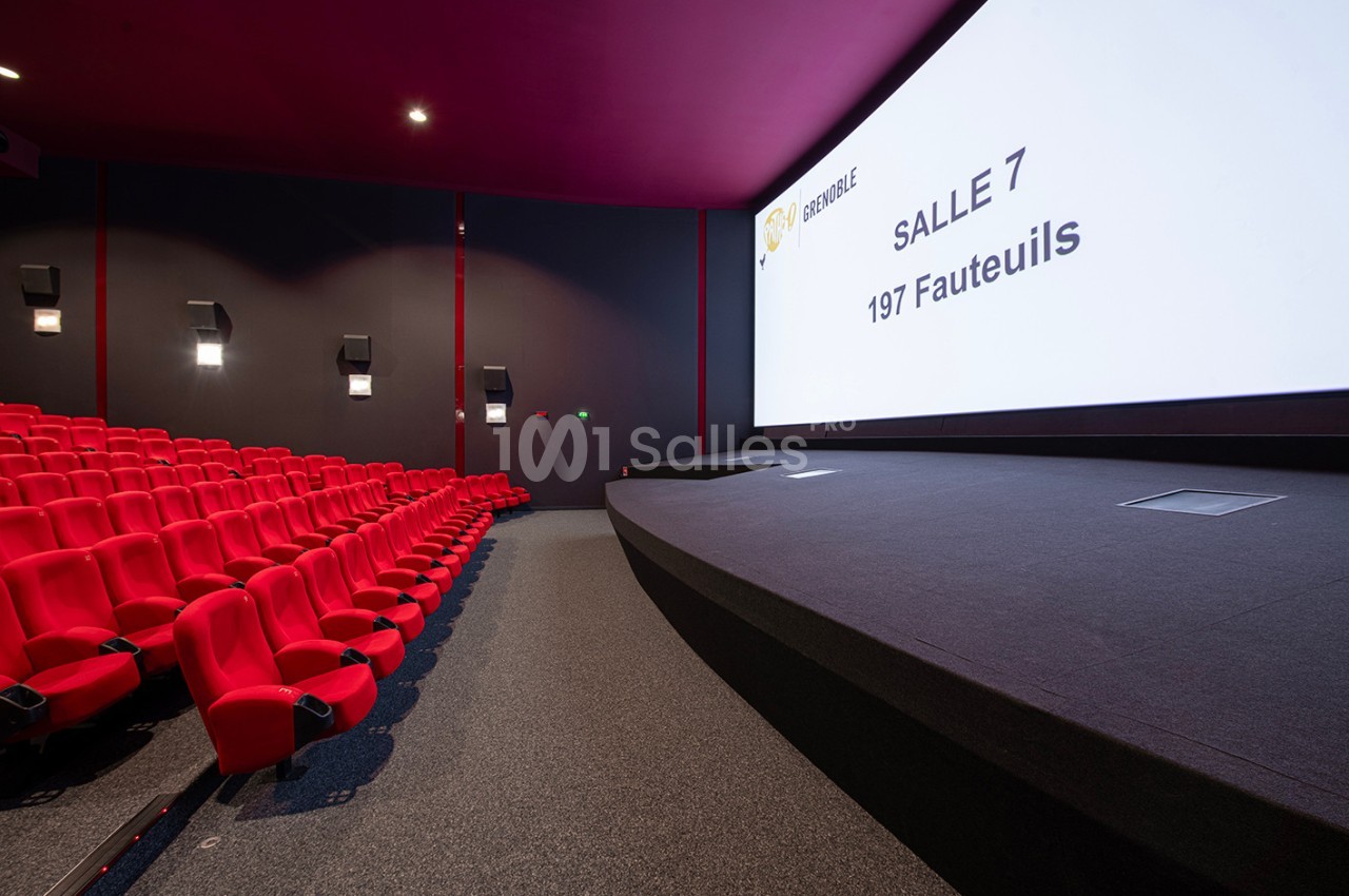 Salle de cinéma moderne avec des rangées de fauteuils rouges et un grand écran affichant ’Salle 7 - 197 fauteuils’.