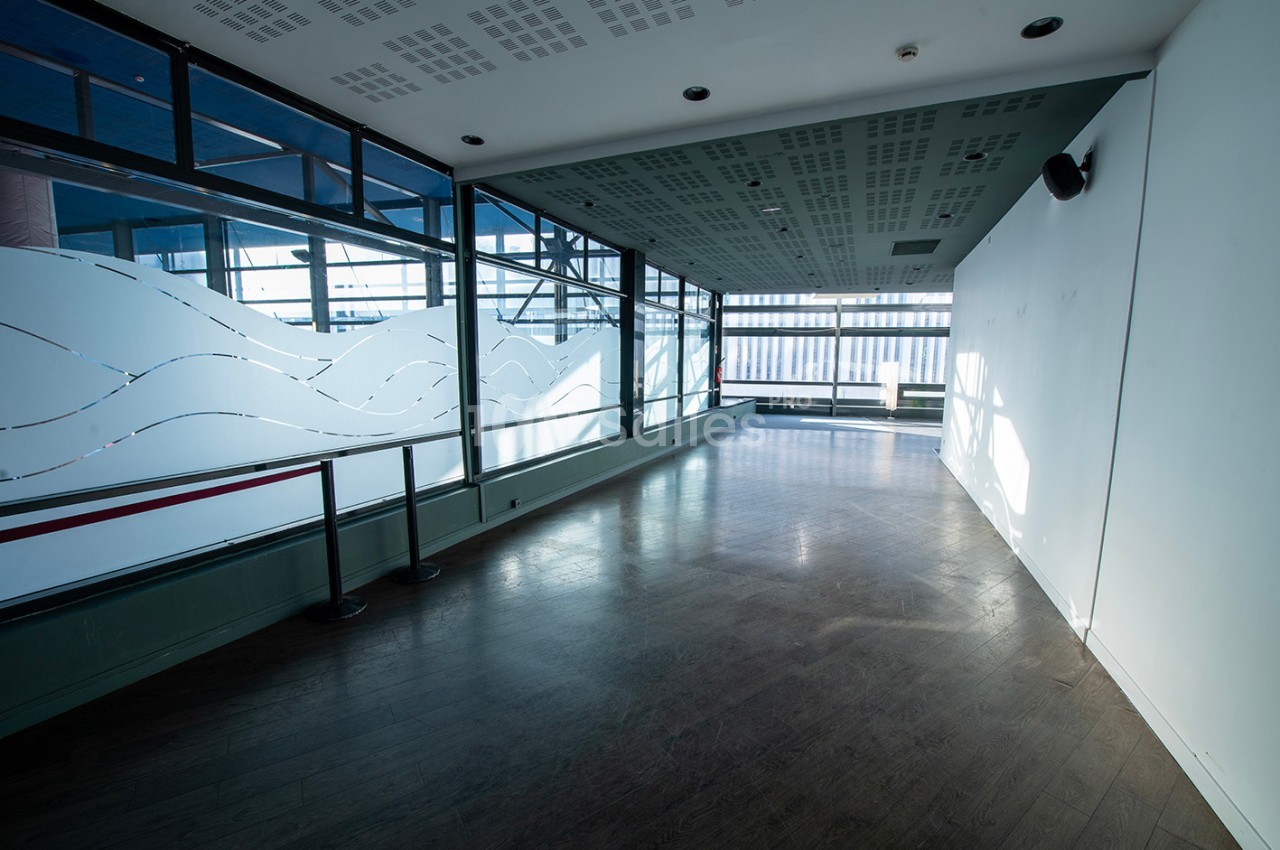 Salle lumineuse avec parquet sombre, grandes baies vitrées et panneaux décoratifs translucides aux motifs ondulés.
