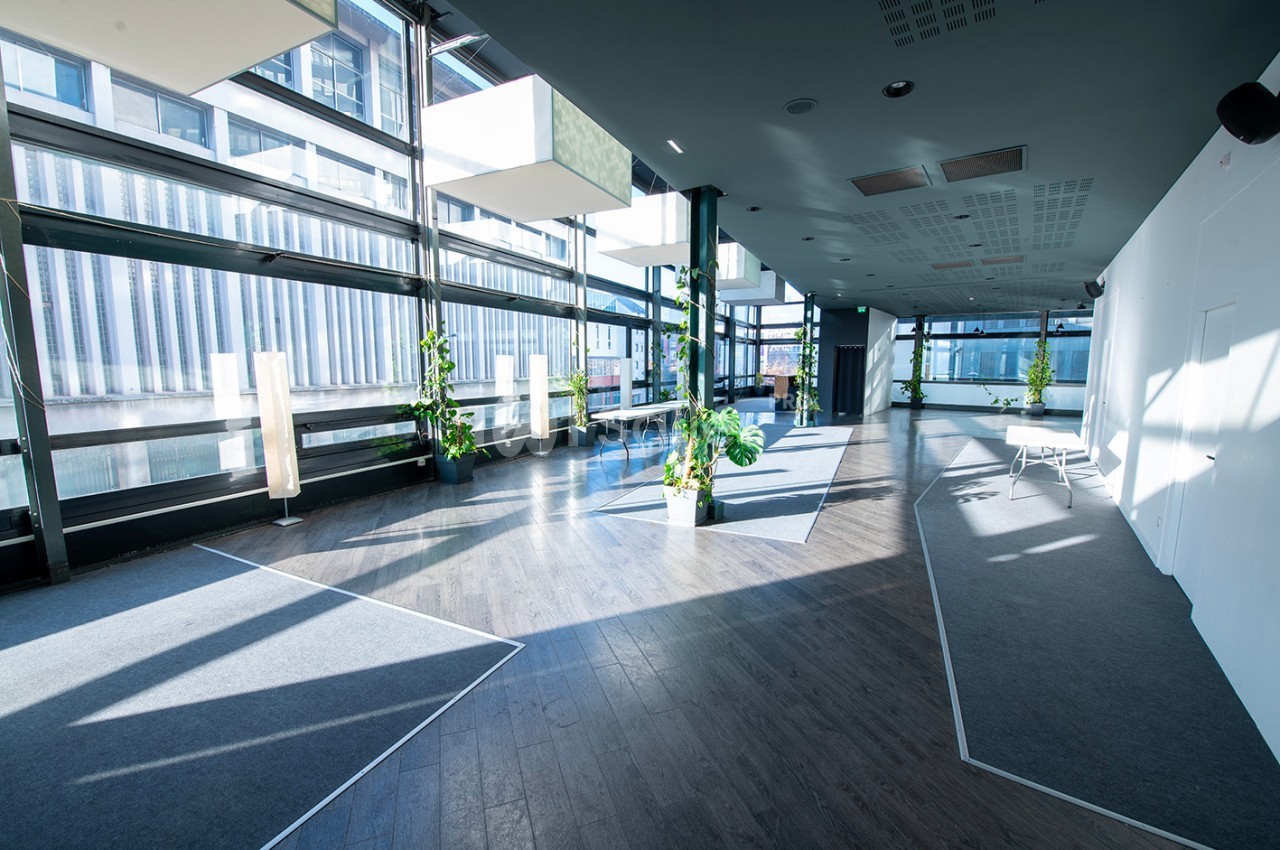 Salle lumineuse avec de grandes baies vitrées, sol en bois, plantes décoratives et mobilier minimaliste.