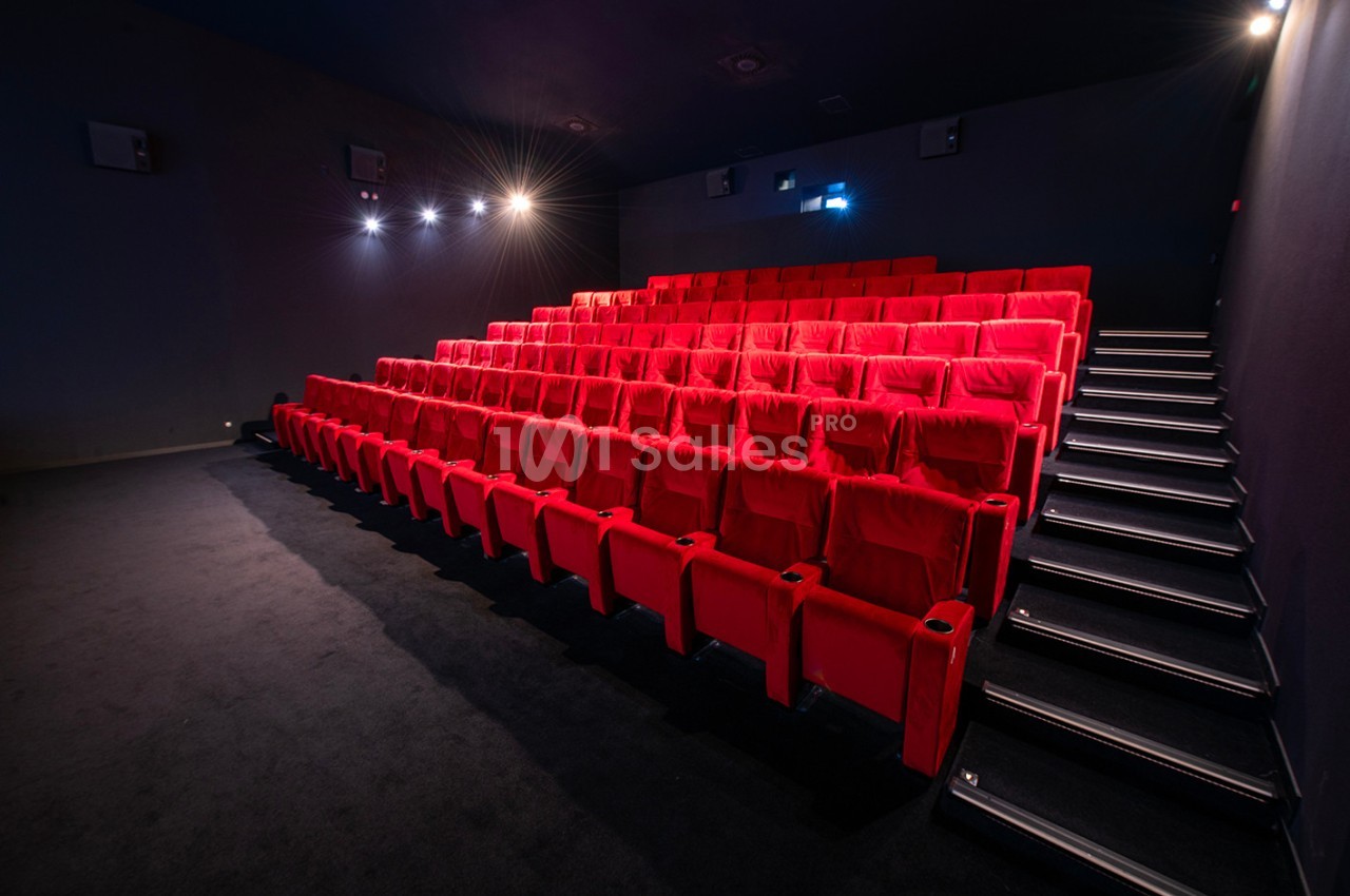 Salle de cinéma vide avec des rangées de fauteuils rouges et un éclairage tamisé.