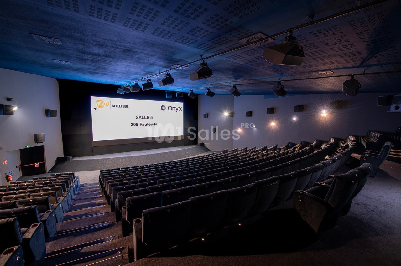 Salle de cinéma moderne avec écran allumé, rangées de fauteuils noirs et éclairage mural discret.