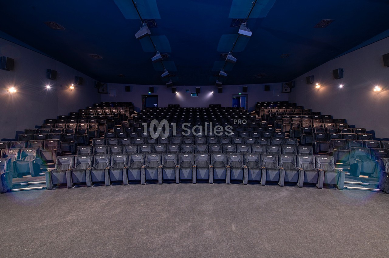 Salle de cinéma vide avec des rangées de sièges noirs alignés et un éclairage tamisé.