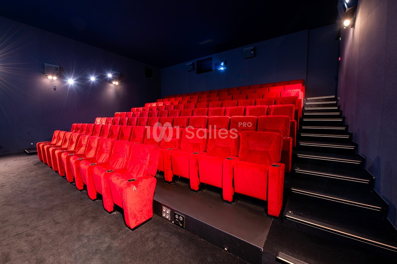 Salle de cinéma vide avec des rangées de sièges rouges et un éclairage tamisé.